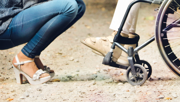 Ein Rollstuhl und Füsse in Stöckelschuhe auf Mergelweg