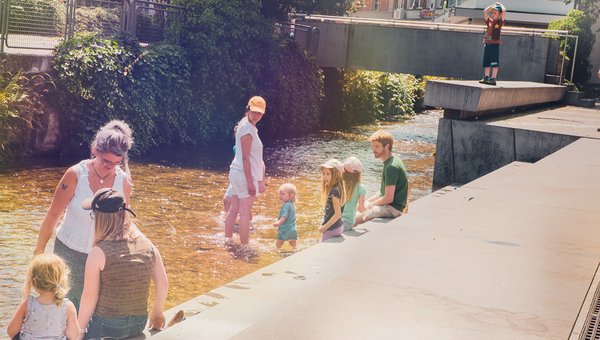 Gruppe von Eltern und Kindern sind sich im Fluss die Füsse am Abkühlen