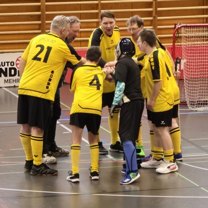 Das Unihockeyteam steht auf dem Spielfeld im Kreis und alle halten die Hände in die Mitte des Kreises.